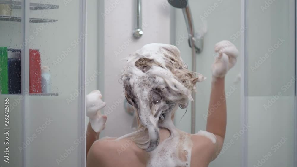 Young girl bathing under a shower at home - back view. Beautiful teen girl taking shower and washing in the bathroom. Happy child washing head, face and body with water. Stock ビデオ | Adobe Stock