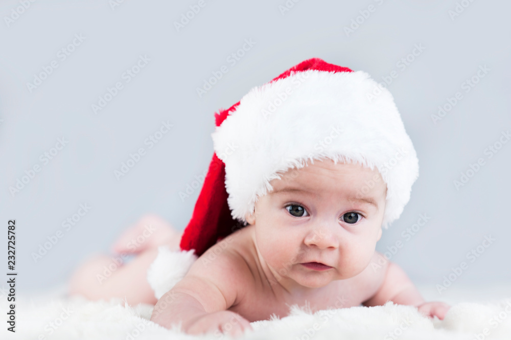 very beautiful bright emotional happy little baby in Santa hat crawling on white plaid very beautiful bright emotional happy little baby in Santa hat crawling on white plaid