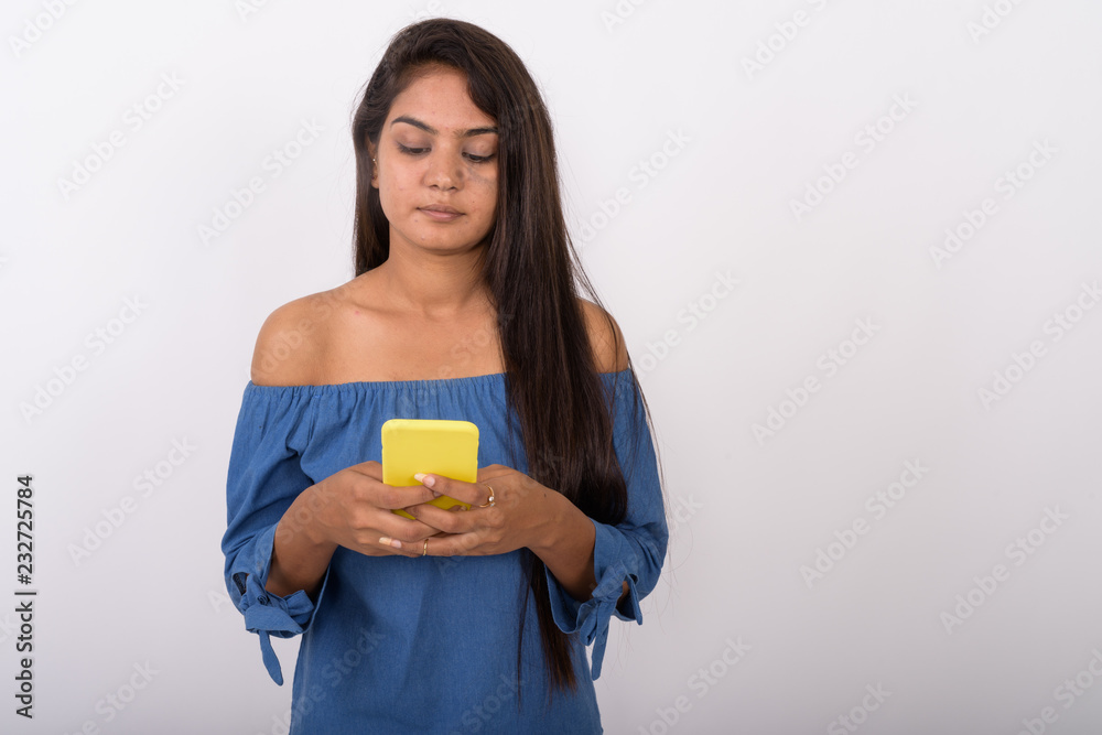 Studio shot of young Indian woman using mobile phone against whi Studio shot of young Indian woman using mobile phone against whi