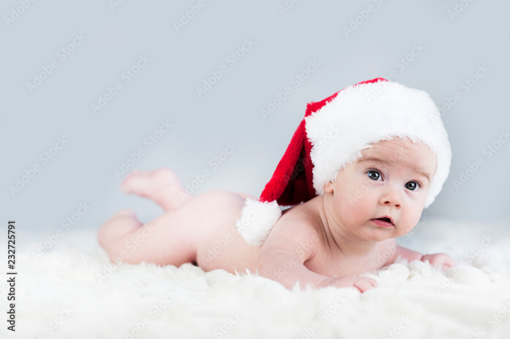 very beautiful bright emotional happy little baby in Santa hat crawling on white plaid very beautiful bright emotional happy little baby in Santa hat crawling on white plaid
