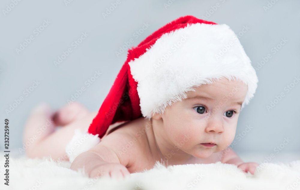 very beautiful bright emotional happy little baby in Santa hat crawling on white plaid very beautiful bright emotional happy little baby in Santa hat crawling on white plaid