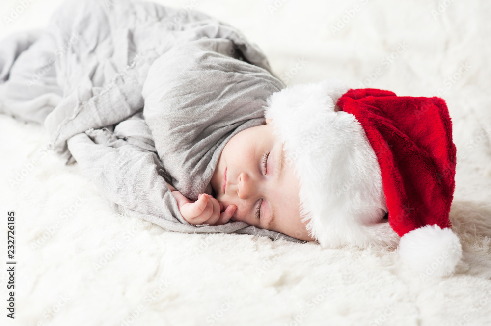 very beautiful bright happy little baby in Santa hat sleeping on white plaid wrapped in grey fabric on black background