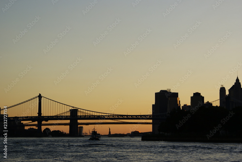 Silhouette of the Statue of Liberty and the Brooklyn Bridge at sunset.