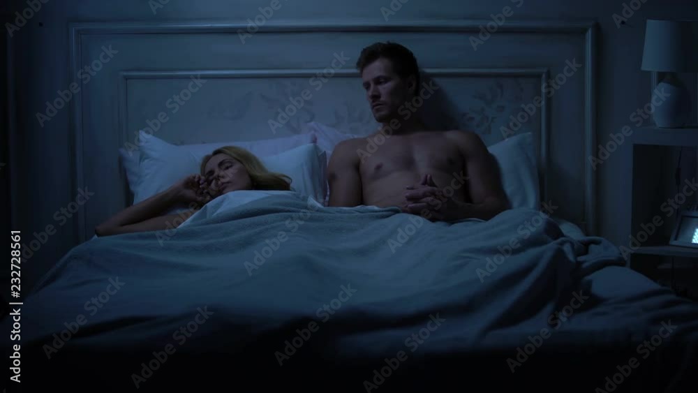 Disappointed man sitting in bed near sleeping spouse after quarrel, family fight