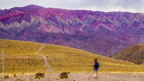 A young woman wearing shorts and a backpack approaches the Serranias de Hornocal (Cerro de Catorce Colores) mountains in the UNESCO-listed Quebrada de Humahuaca valley in north western Argentina