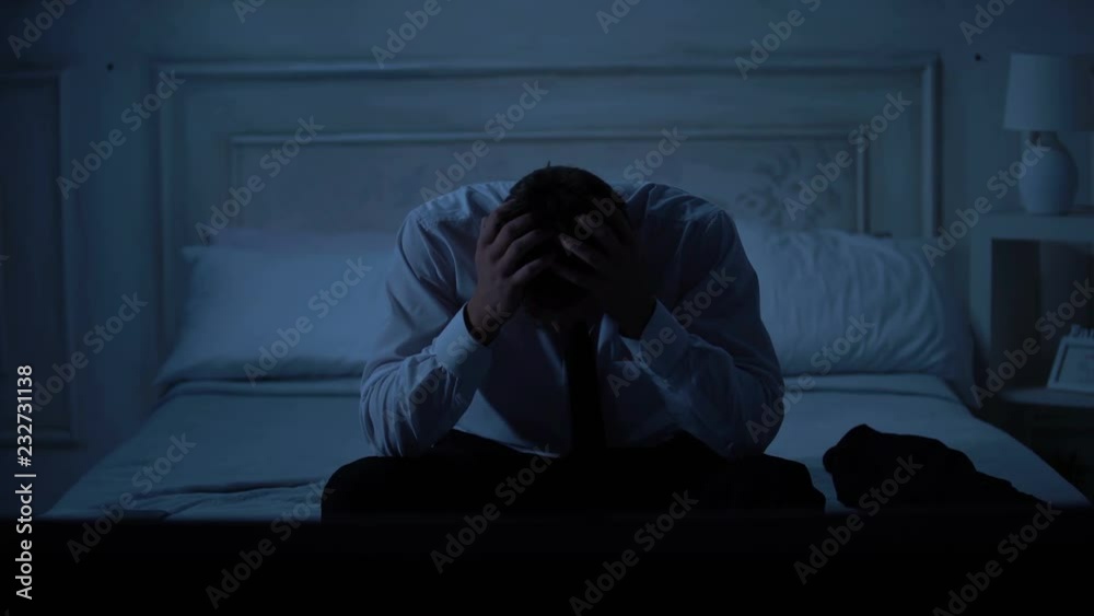 Anxious handsome male in business suit sitting on bed, rubbing hands, problems Anxious handsome male in business suit sitting on bed, rubbing hands, problems