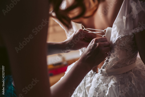 A friend helps the bride to tie a white wedding dress © Semenova Jenny