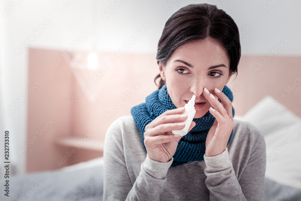 Body weakness. Close up of ill upset woman dripping her nose with nasal drops while averting her eyes Body weakness. Close up of ill upset woman dripping her nose with nasal drops while averting her eyes