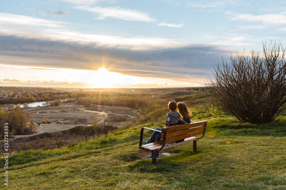 Fototapeta premium Woman and child sitting on a bench admiring the sunset
