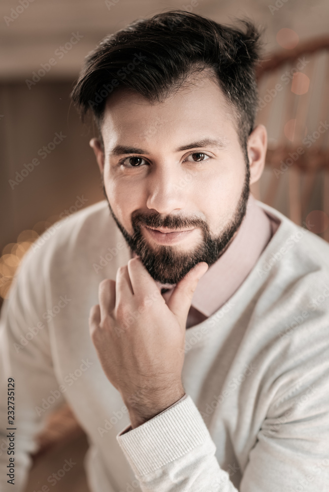 Fototapeta premium Feeling success. Attractive brunette keeping smile on his face and touching beard while being high spirited
