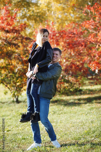 Young guy holds a girl in his arms in the autumn park. Fall. Young Man and Woman outside. Happy family Concept. Yellow Trees and Leaves. © olgasparrow