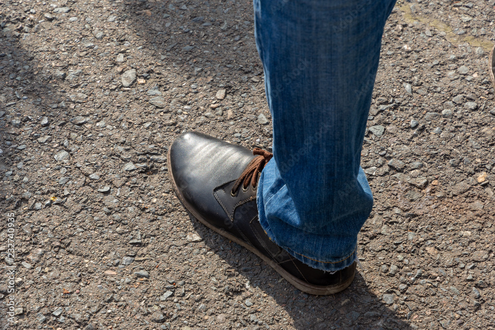 fashion man's leg in jeans and brown leather boot are on asphalt pavement