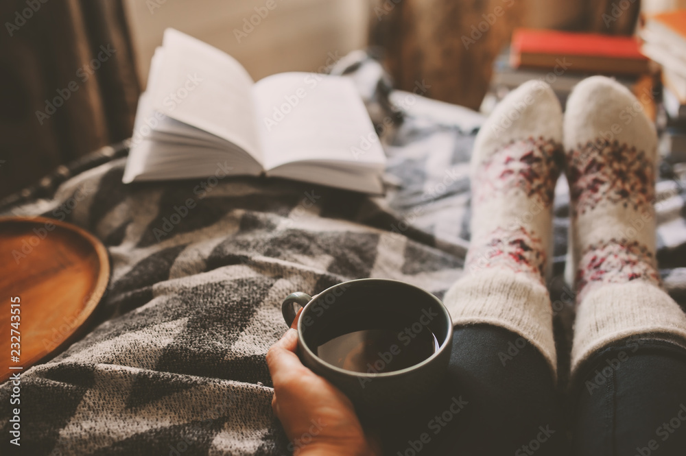 cozy winter day at home with cup of hot tea, book and warm socks. Spending weekend in bed, seasonal holidays and hygge concept - obrazy, fototapety, plakaty 