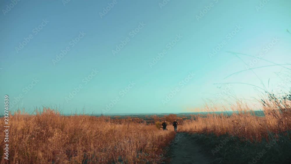 Two men hikers traveler hiking with backpacks are walking along the path climbing into the mountains. slow motion video. Tourist Hipster Hiker traveler on background view blue sky clouds go hiking