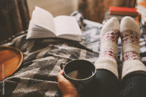 cozy winter day at home with cup of hot tea, book and warm socks. Spending weekend in bed, seasonal holidays and hygge concept photo