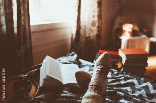 cozy winter day at home with cup of hot tea, book and warm socks. Spending weekend in bed, seasonal holidays and hygge concept photo