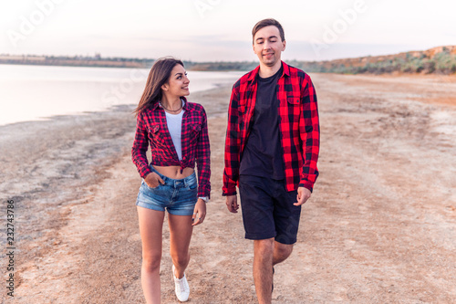 Happy young couple on the beach walking together during sunset. Date outdoors. They look happy