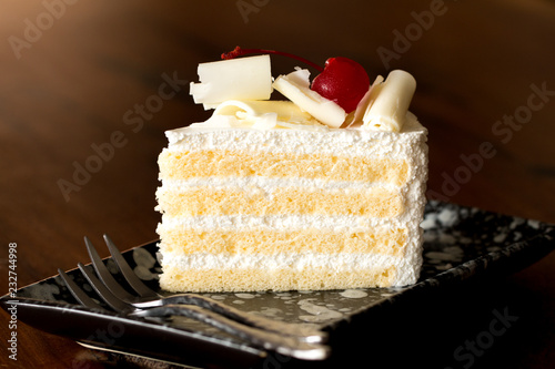 Piece of white cake with vanilla frosting and cherry jelly  topped with white cheese