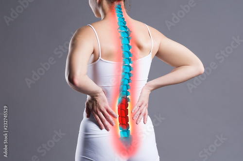 Pain in the spine, woman with backache on gray background, back injury photo