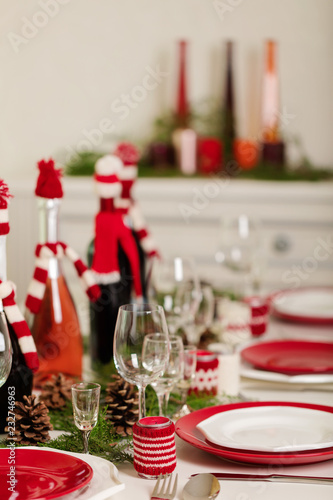 Merry Christmas and Happy New Year! Тable setting holiday knitted decor - Santa Claus knitted hats on the bottle with wine, candles in candlesticks in knitted decor.