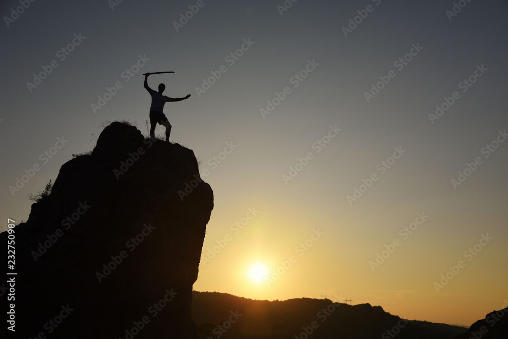 Silhouette of a man with katana exercising on edge of the cliff