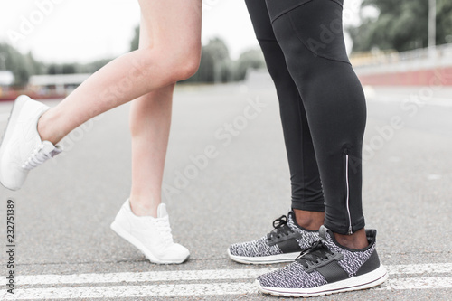 Love sport concept - running couple kissing. Closeup of running shoes and girl standing on toes to kiss boyfriend during jogging workout training outdoors
