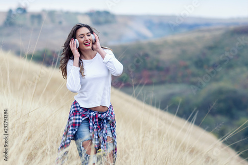 Beautiful long hair woman with headphones in the middle of the field with landscape on background