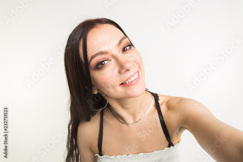 Happy european female model with dark hair enjoying indoor photoshoot. young woman is taking a selfie on white background
