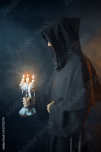 Medieval monk in robe holds a candlestick in hands
