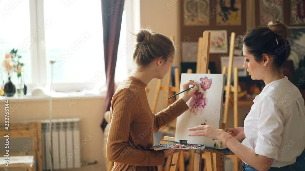Young women art teacher and student are having lesson at painting school, girl is mixing colors on palette while master is giving advice talking to learner. Young women art teacher and student are having lesson at painting school, girl is mixing colors on palette while master is giving advice talking to learner.