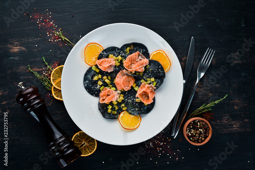 Black ravioli with salmon and parmesan cheese. In a plate on a wooden background. Top view. Free copy space.