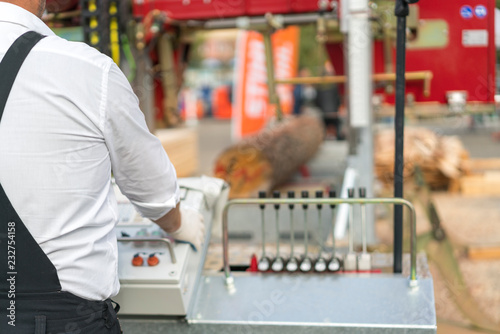 Worker pressing buttons on CNC machine control board in factory. Partially milled log on a portable lumber milling machine. photo