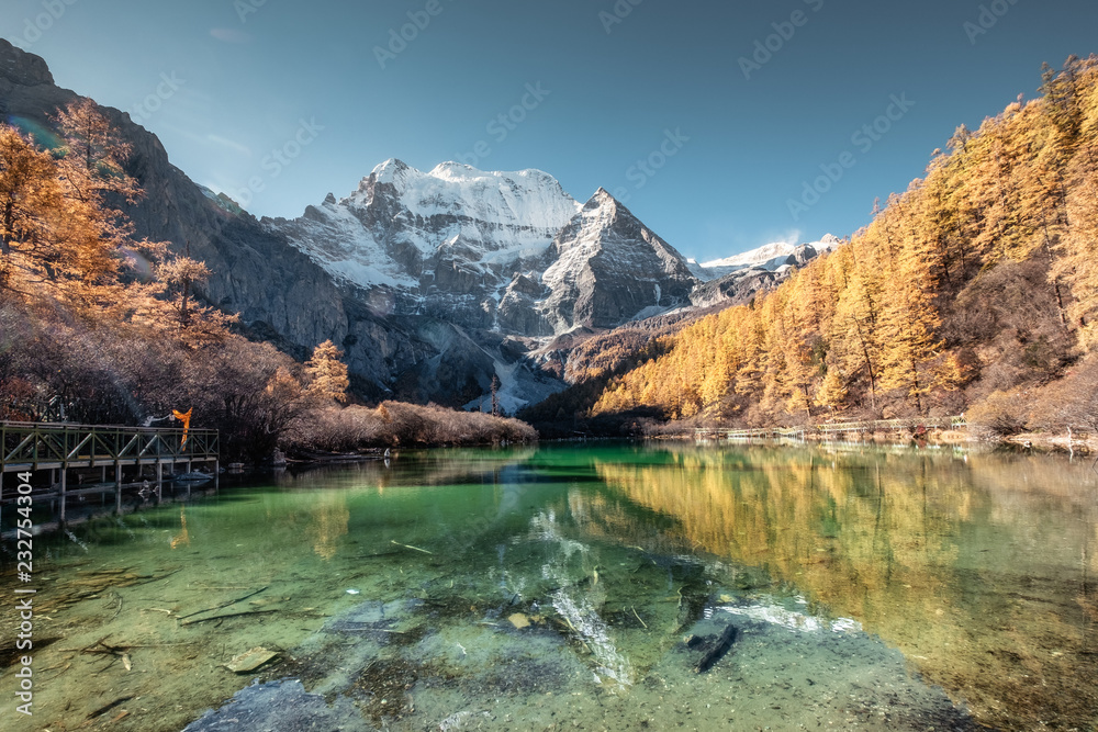 Xiannairi mountain reflection on emerald lake with golden pine forest in autumn