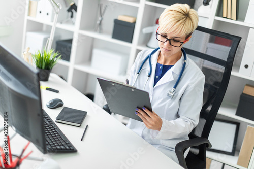 A young girl in a white robe sitting at the table and fills out a document