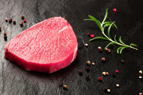A photo of a steak of eye round beef, a raw cut, with rosemary and pepper on a black background with copy space photo