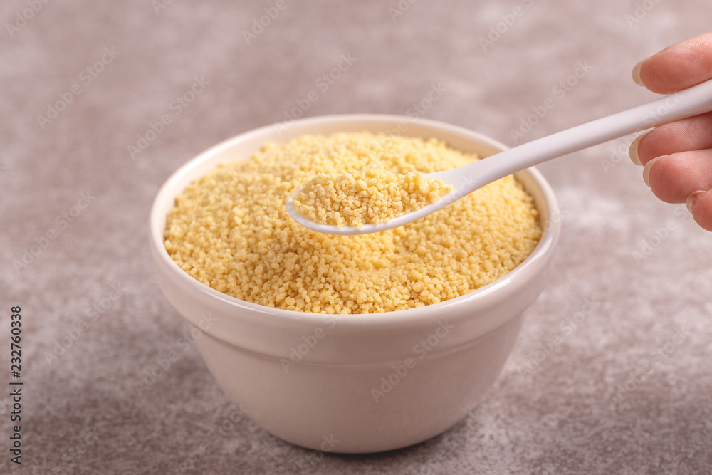Full spoon of raw couscous grain in clay bowl Full spoon of raw couscous grain in clay bowl