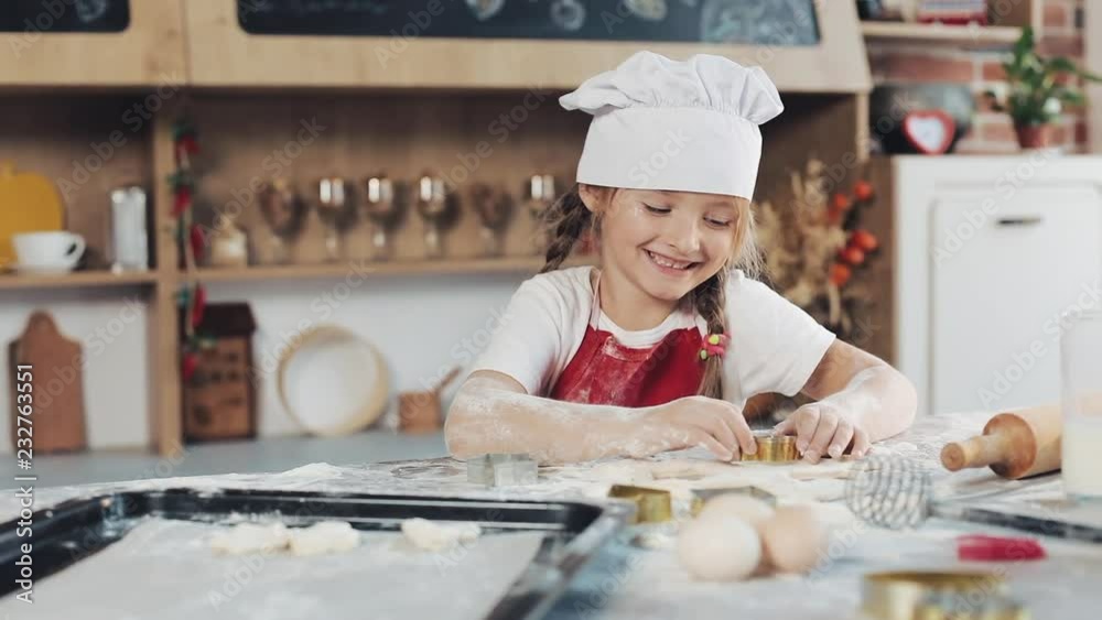Cute small girl making cookies from raw dough in the form of flowers and stars. Little daughter with mother makes cookies at home in the kitchen Cute small girl making cookies from raw dough in the form of flowers and stars. Little daughter with mother makes cookies at home in the kitchen