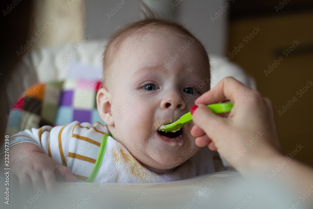 The first feeding of the baby from the spoon. Mom feeds baby