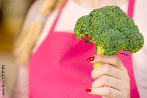 Woman in kitchen holding green fresh broccoli. Housewife cooking. Healthy eating, vegetarian food, dieting and people concept.