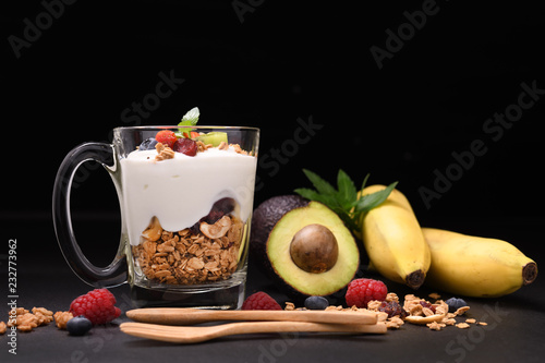 Yogurt with granola and fruits in glass on black granite stone table