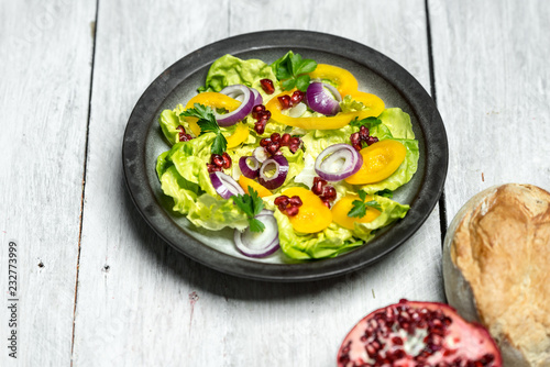 Healthy breakfast, fresh salad with the addition of purple onion and pomegranate seeds on white, wooden background