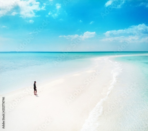 Panoramic aerial photo of a young man walking at the beach by the seashore in small island with white sand and crystal clear blue turquoise water photo