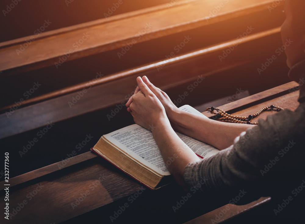 Christian woman praying in church. Hands crossed and Holy Bible on ...