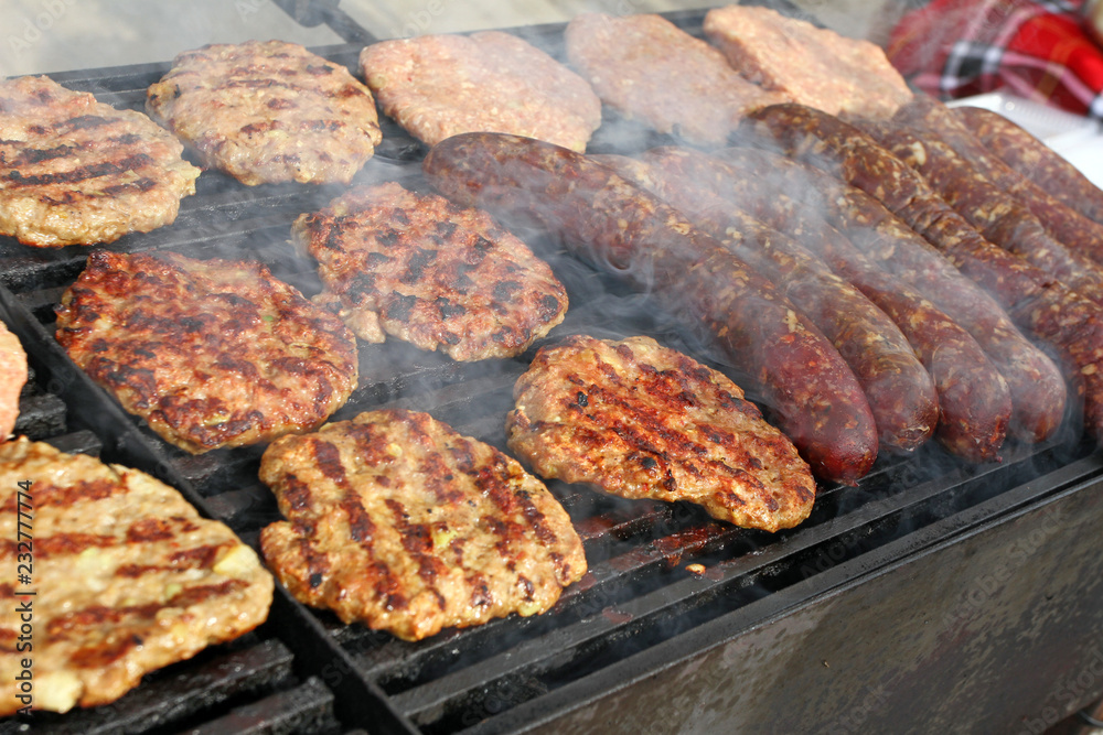 Grilling sausages, burgers, pork steak on barbecues gas grill for party. Hot dogs,sausages and hamburgers on a barbeque, bbq. Smokes meat food outdoors, fast food. Hamburgers. Pleskavitsa