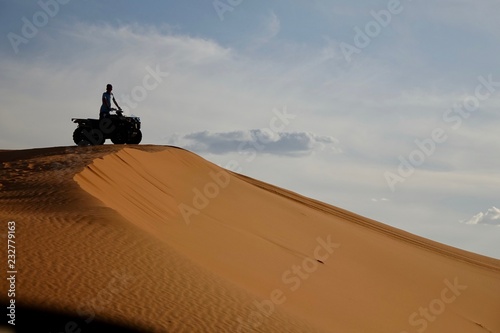 The silhouette of the man on the 4x4 is on the top of the sand dune. The one second before riding down. Sunset at the Sahara desert. photo