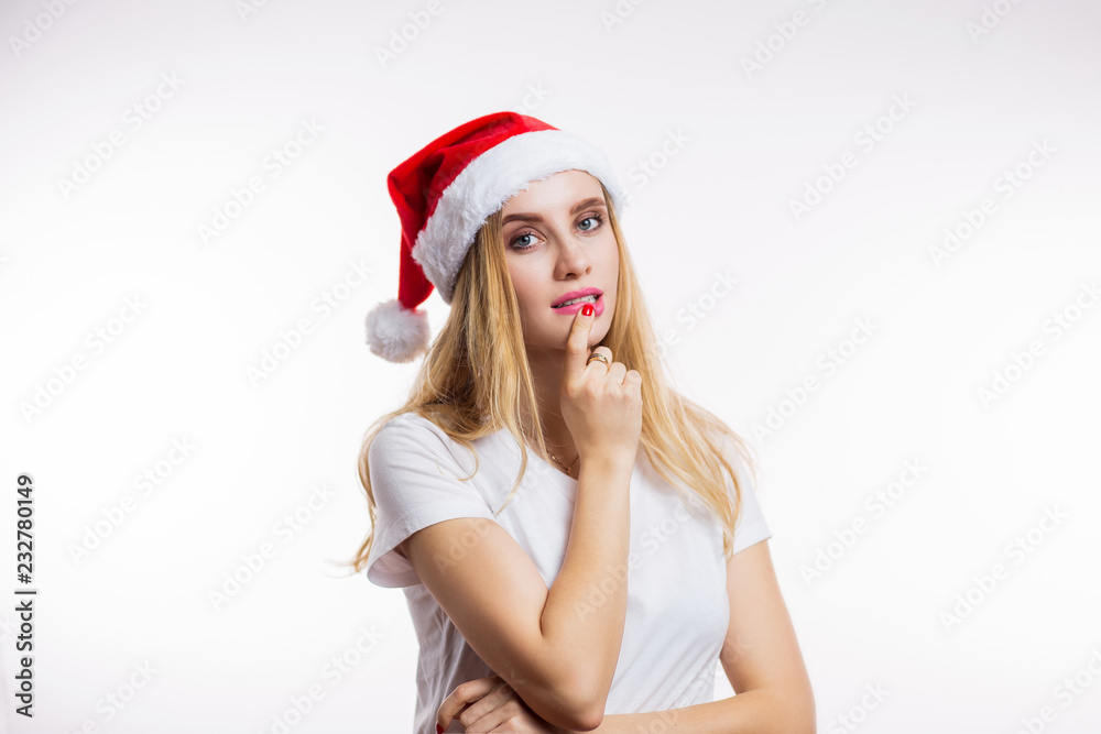 Charming blonde woman in Santa hat looks at camera and thinks on white background Charming blonde woman in Santa hat looks at camera and thinks on white background