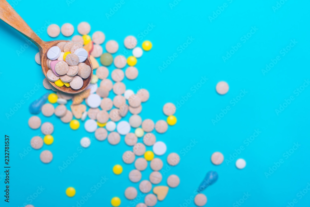 Top view of pharmaceutical medicine pills, capsules and tablets w/ wooden spoon on light blue background. Vitamin and supplement. Health behavior concept. Minimal style. Creative idea.
