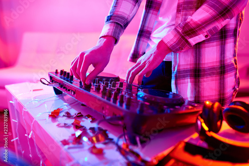 Faceless shot of man in shirt playing music on DJ mixer celebrating New Year on party