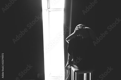 The social theme female loneliness pain suffering. Abastration male violence family. A young beautiful Caucasian woman in black clothes sitting on three chairs in large dark room. Srach and despair