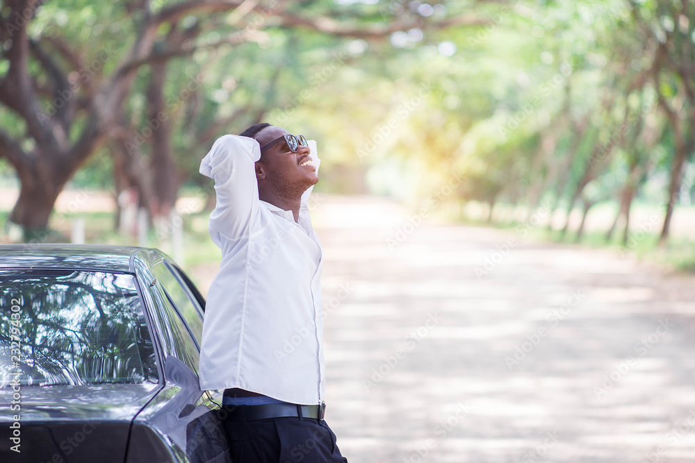 African businessman wearing a white shirt and black glasses stands smiling at the car with happy and relax African businessman wearing a white shirt and black glasses stands smiling at the car with happy and relax